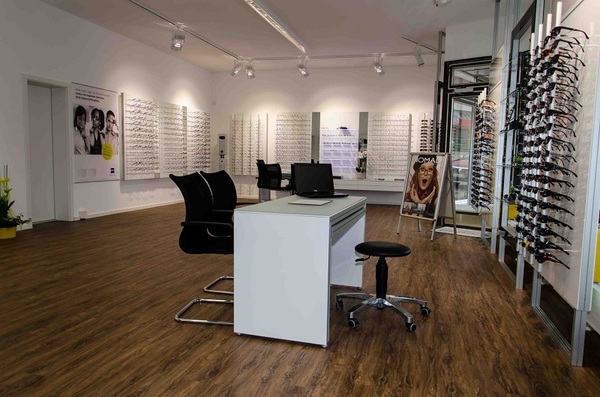 Modernes Optikergeschäft mit zahlreichen Brillengestellen, Beratungstisch und Holzfußboden.